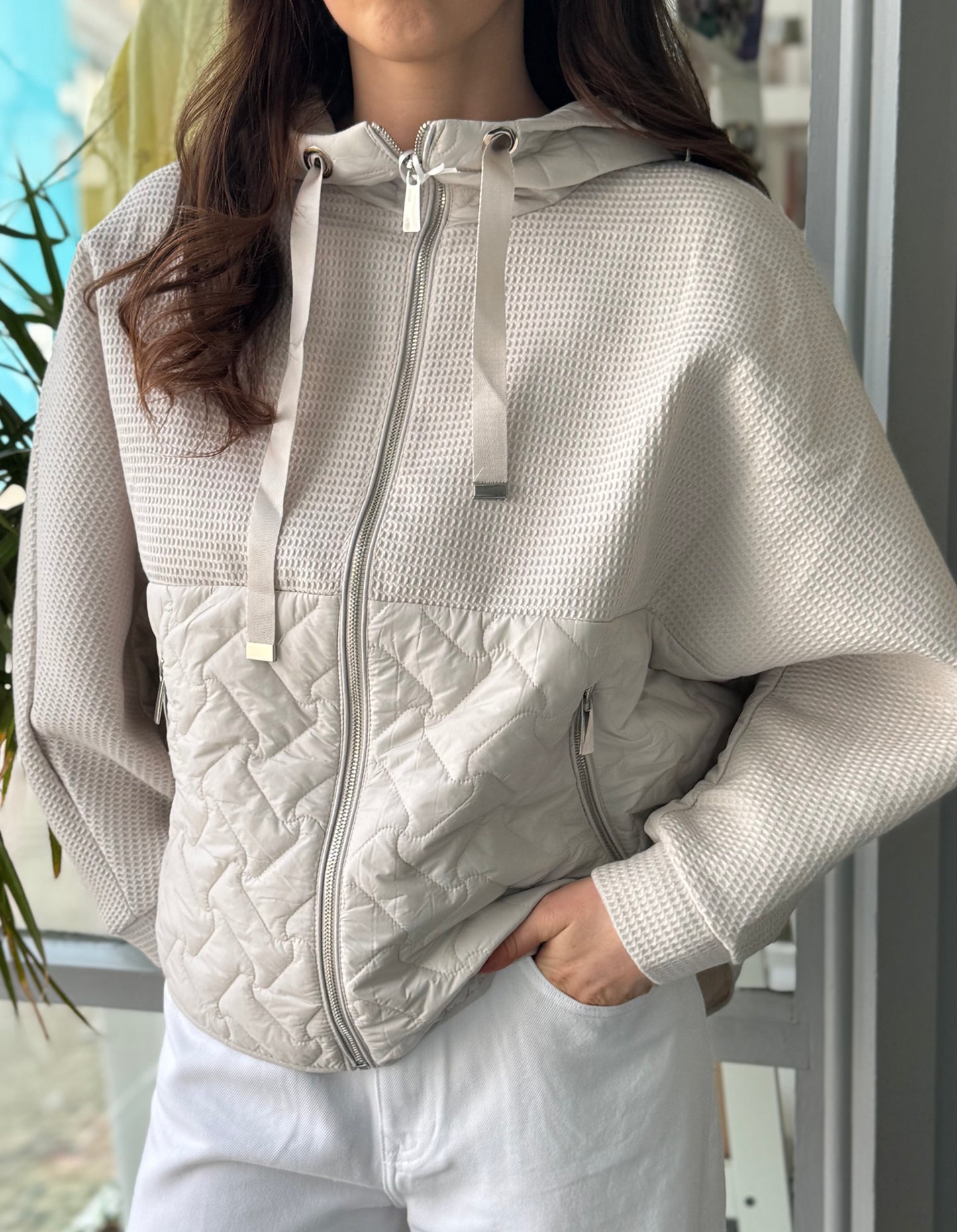 Person wearing a light gray quilted jacket with a blurred outdoor background