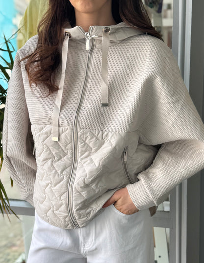 Person wearing a light gray quilted jacket with a blurred outdoor background