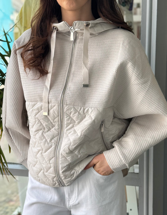Person wearing a light gray quilted jacket with a blurred outdoor background