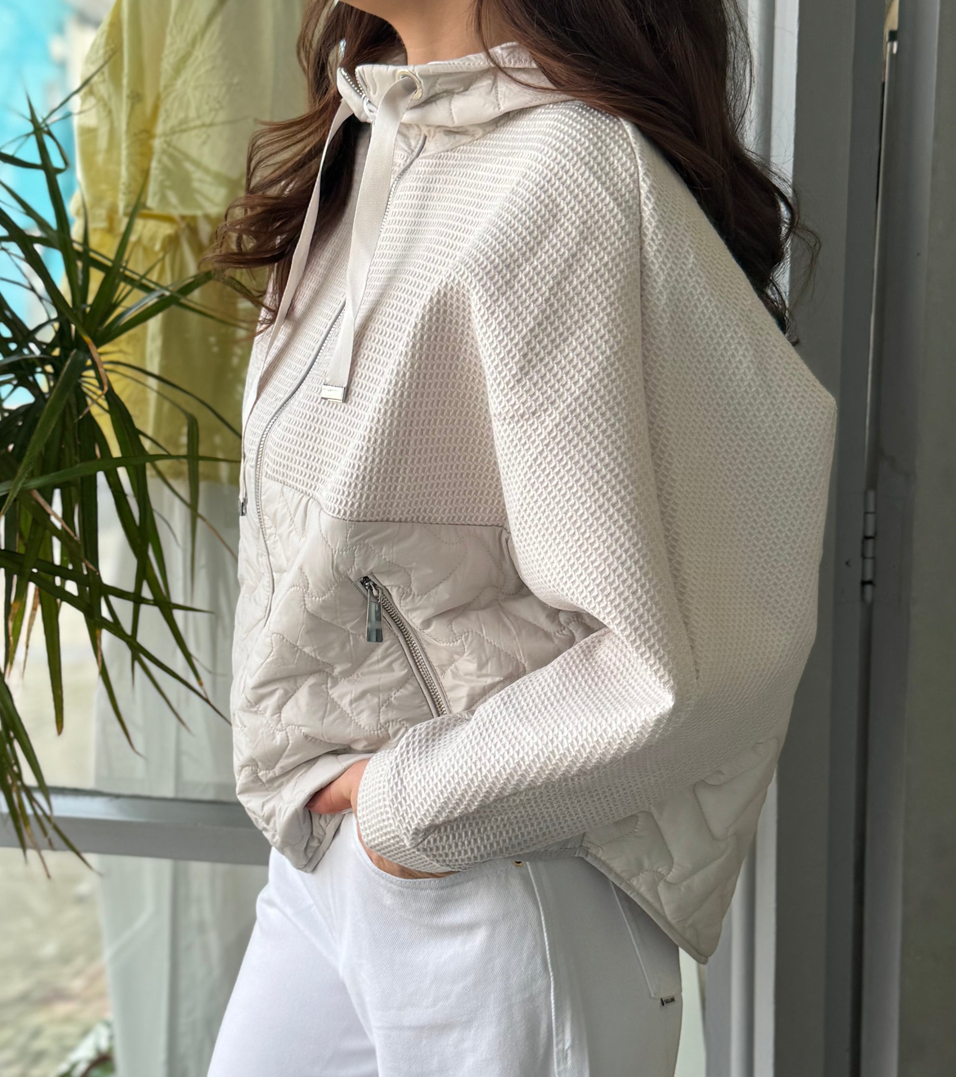 Person wearing a light-colored puffer jacket standing indoors with a plant in the background