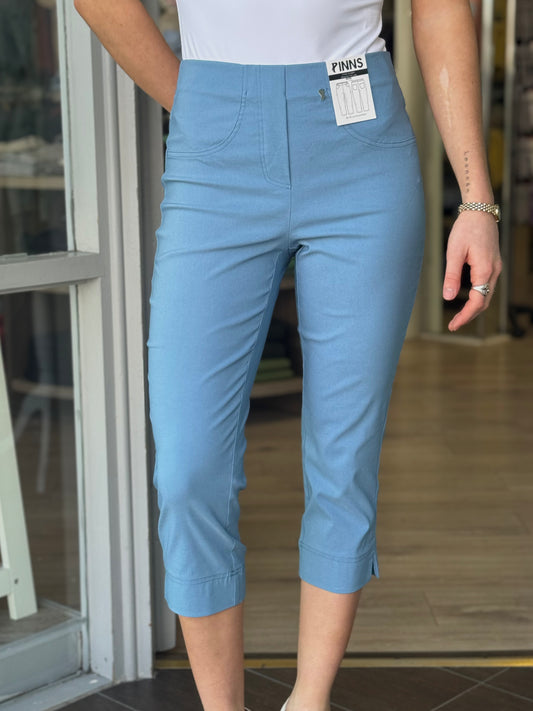 Person wearing blue capri pants with a visible brand tag indoors.