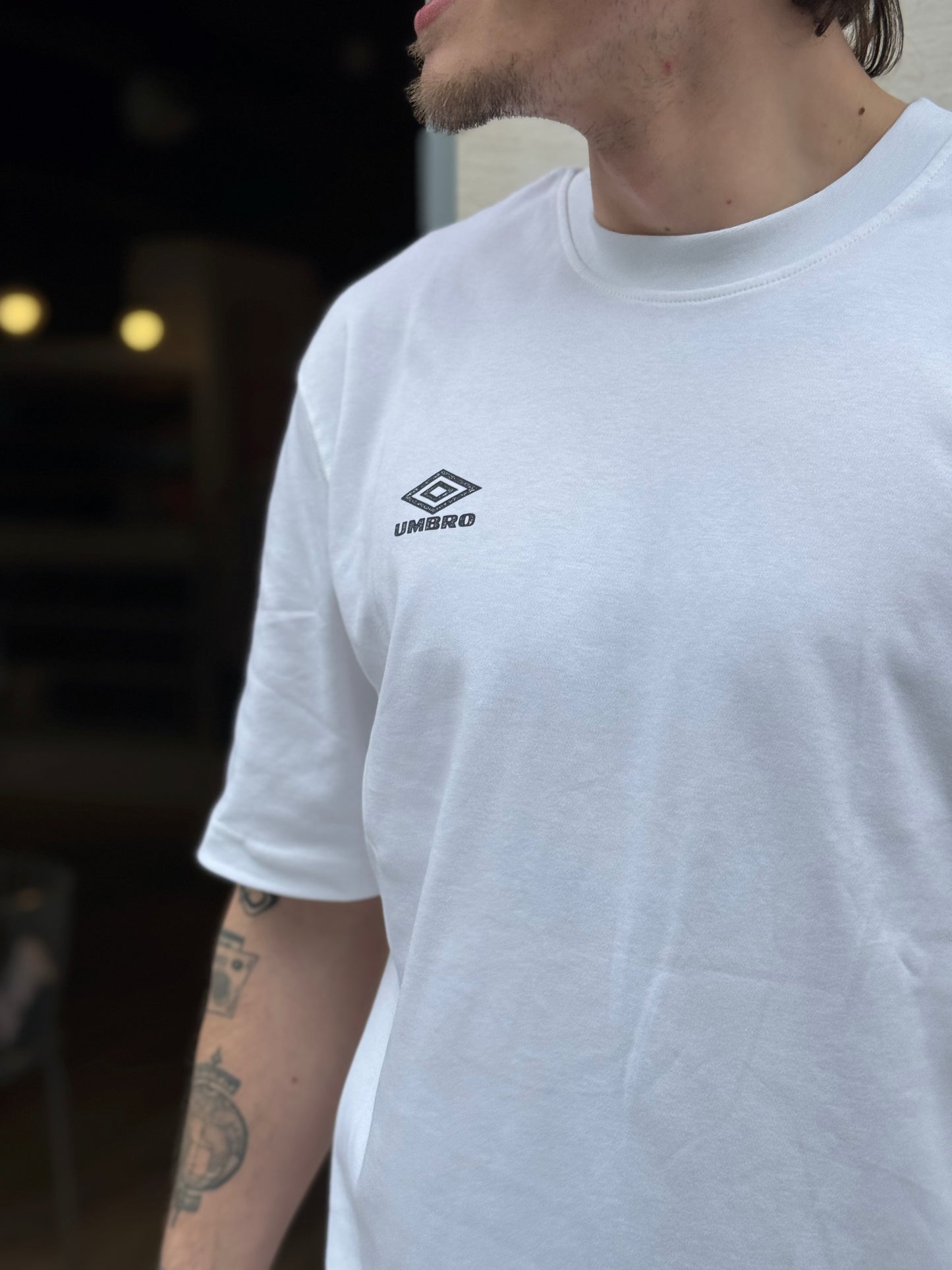 Person wearing a white Umbro t-shirt with a blurred background