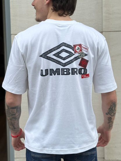 Person wearing a white Umbro t-shirt with logos on the back, standing against a light-colored wall.