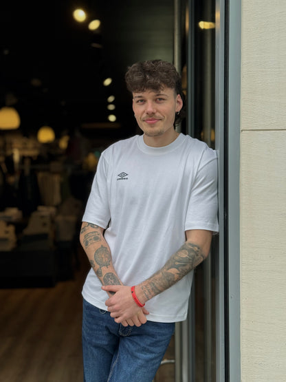 Man wearing a white t-shirt with a logo, standing indoors.