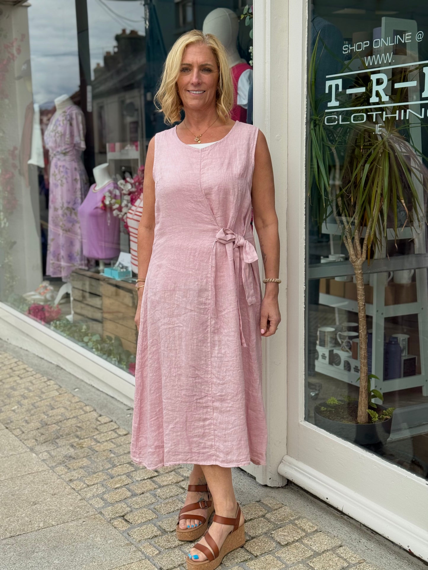 Woman in a pink dress standing outside a clothing store.