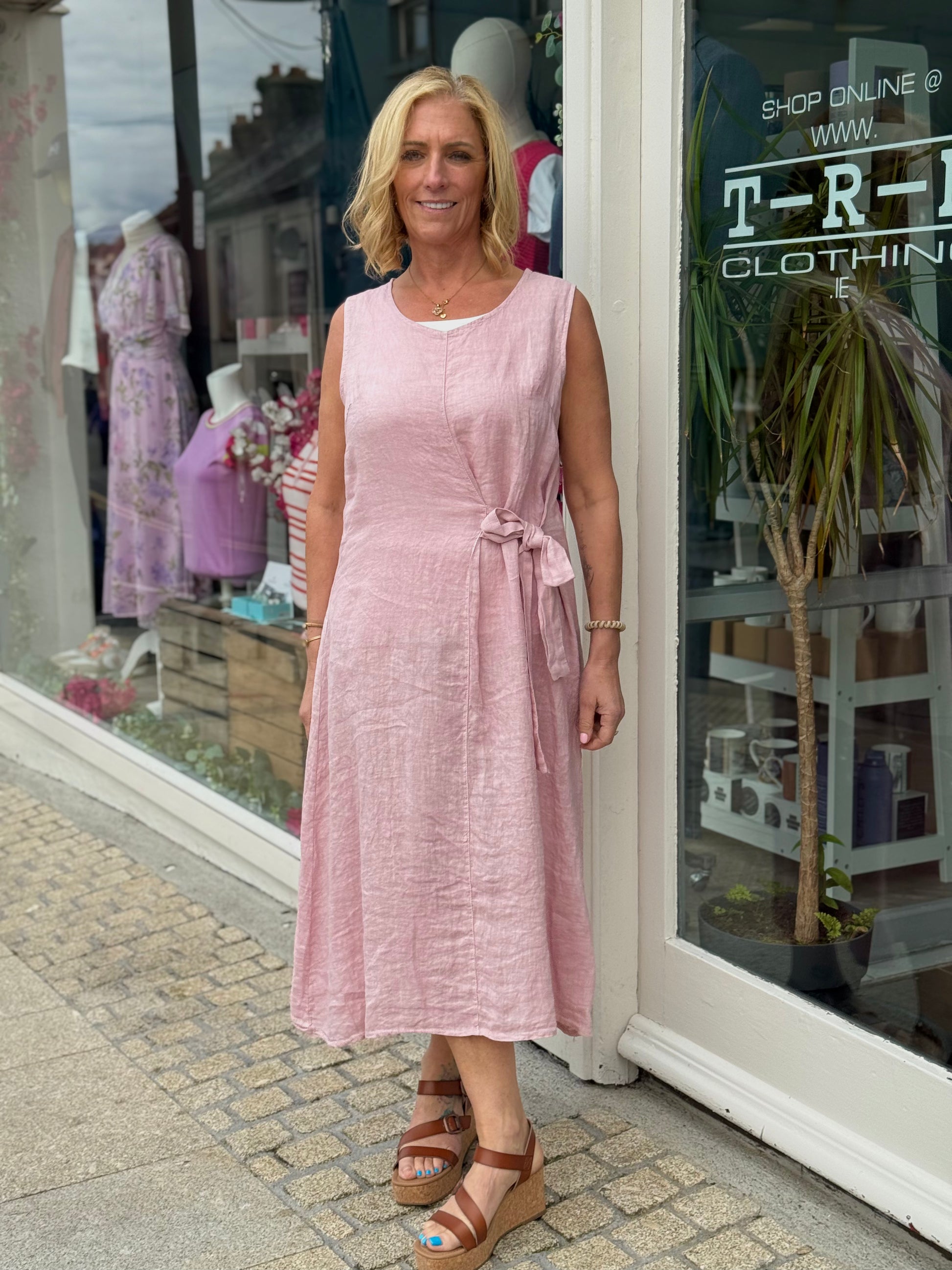 Woman in a pink dress standing outside a clothing store.