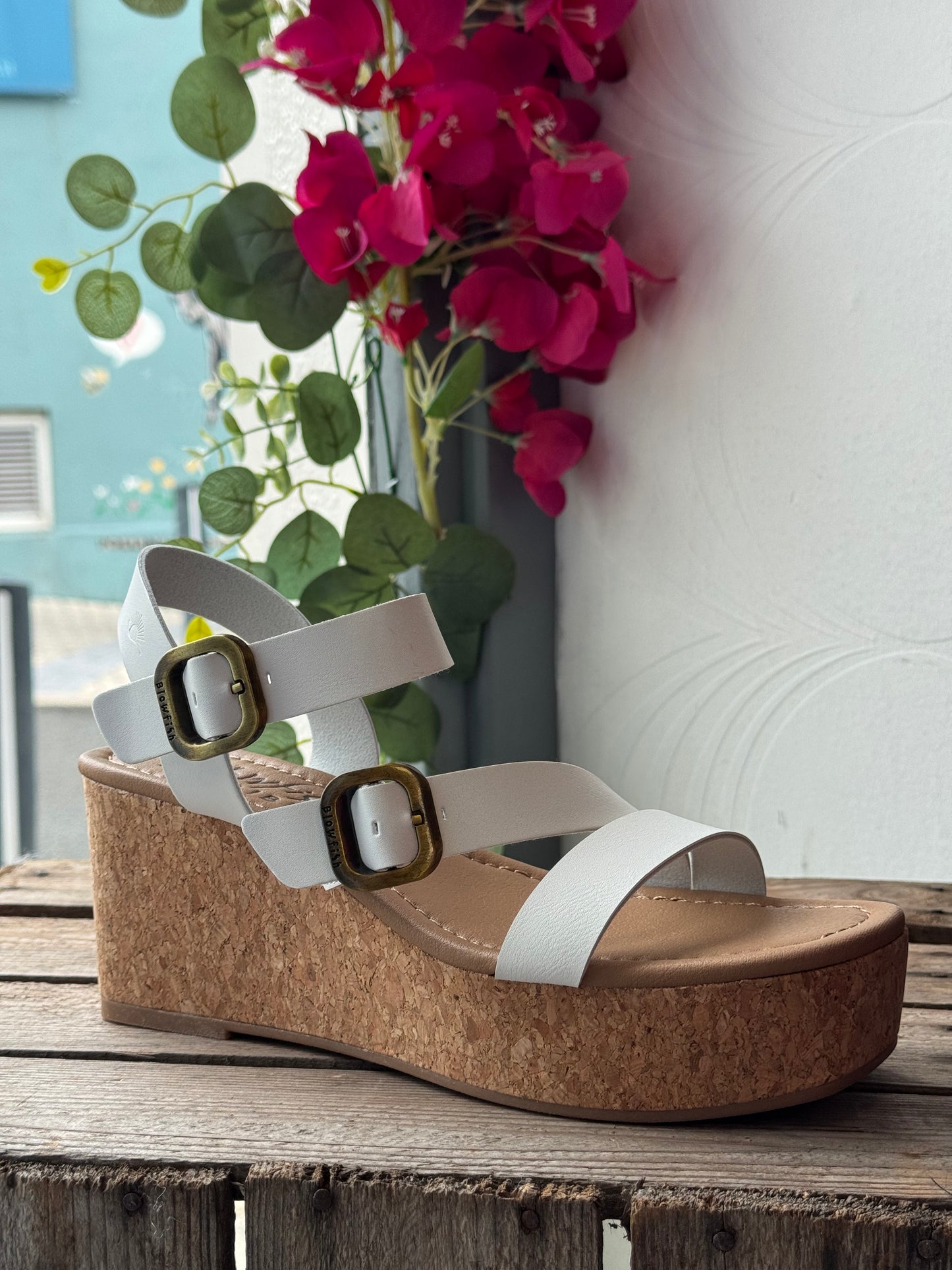 Wedge sandal with cork sole on a wooden surface with flowers in the background