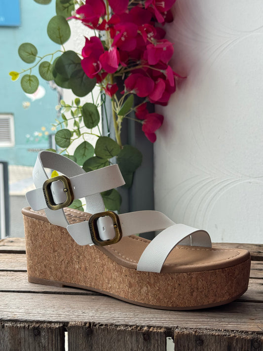 Wedge sandal with cork sole on a wooden surface with flowers in the background
