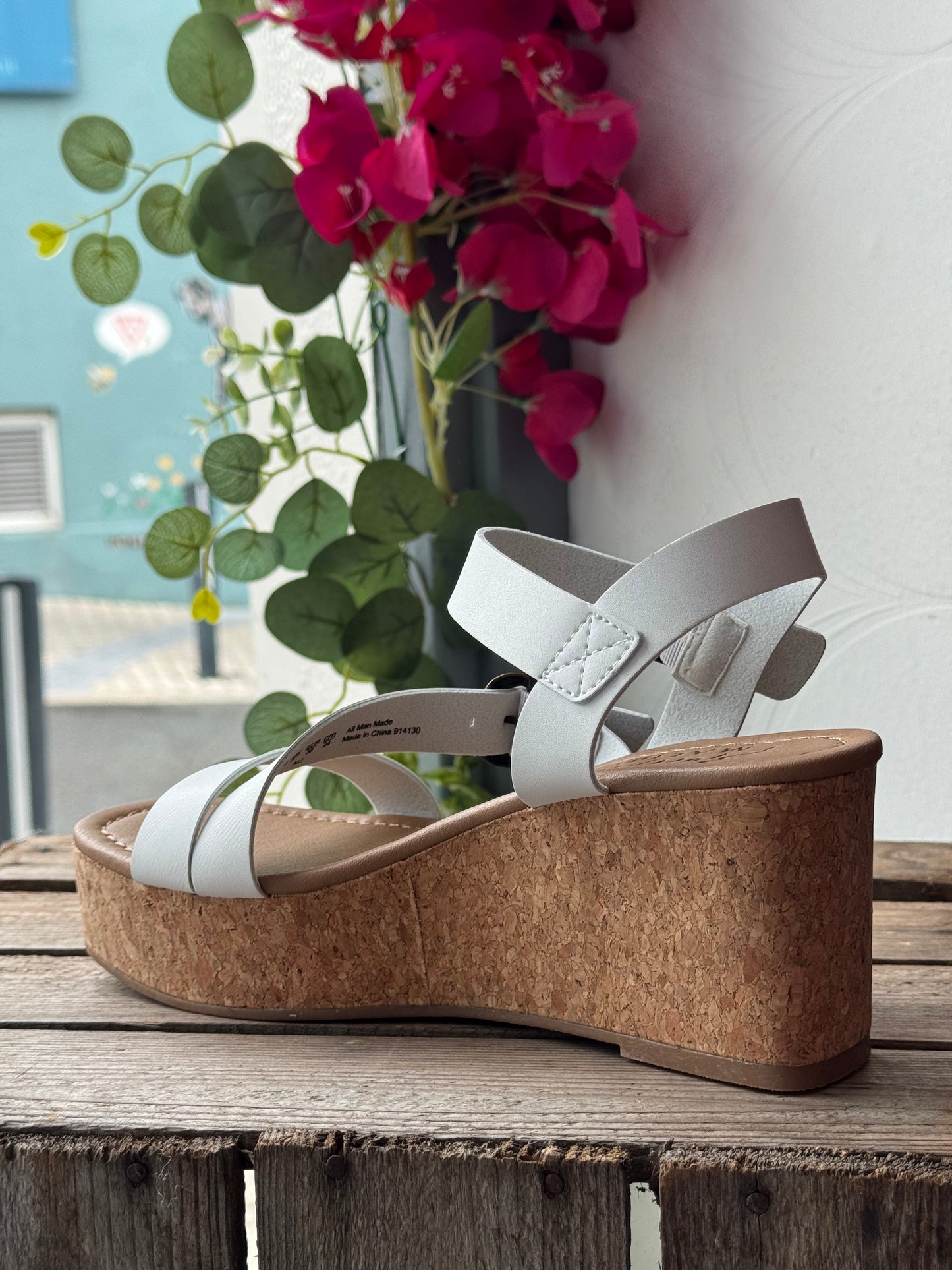 White wedge sandal with cork sole on a wooden surface with flowers in the background