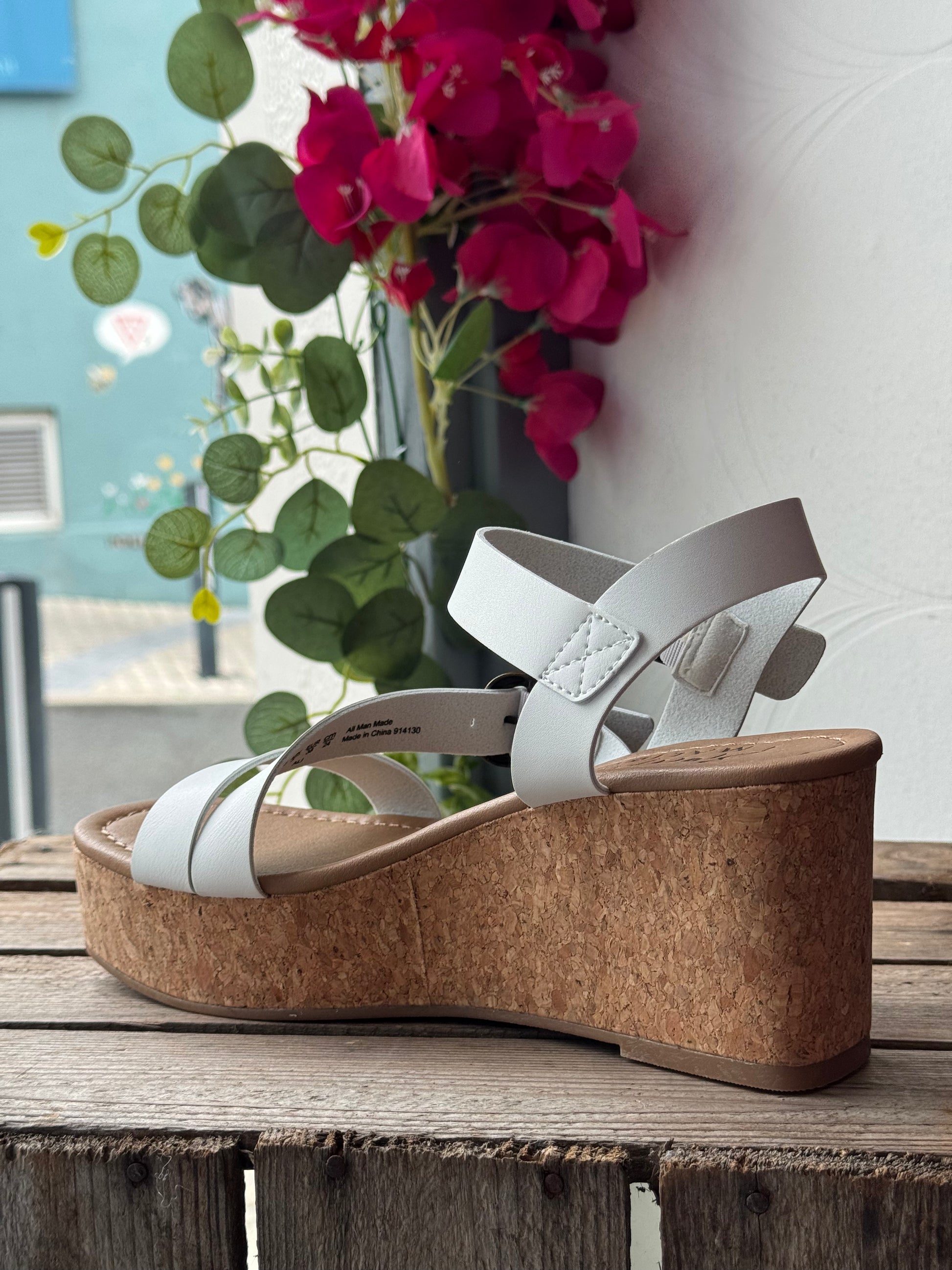 White wedge sandal with cork sole on a wooden surface with flowers in the background