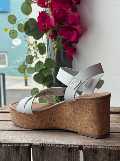 White wedge sandal with cork sole on a wooden surface with flowers in the background