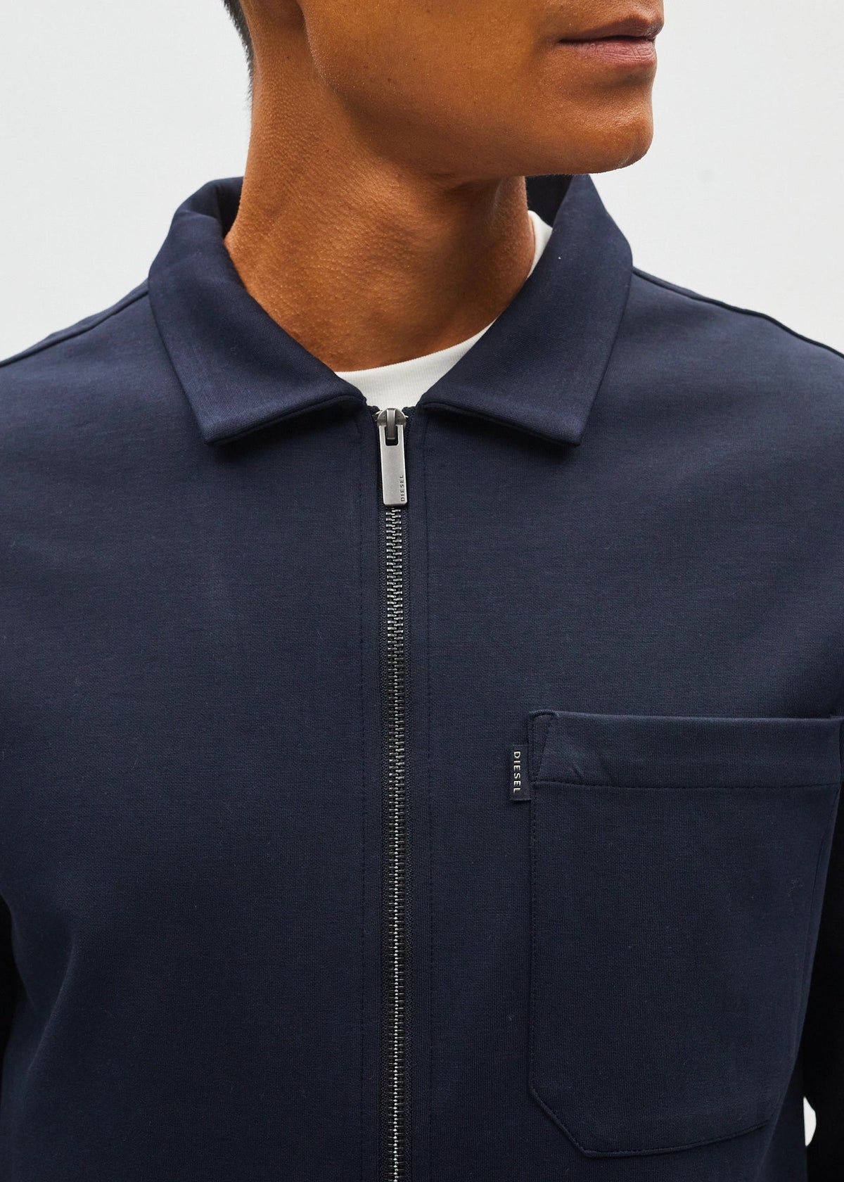 Close-up of a person wearing a navy blue zip-up jacket with a collar and a chest pocket, layered over a white undershirt.