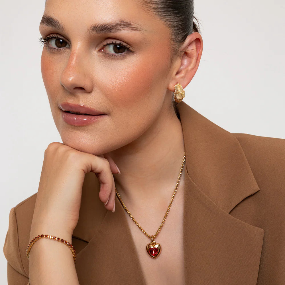 Woman wearing gold jewelry including earrings, necklace, and bracelet against a neutral background