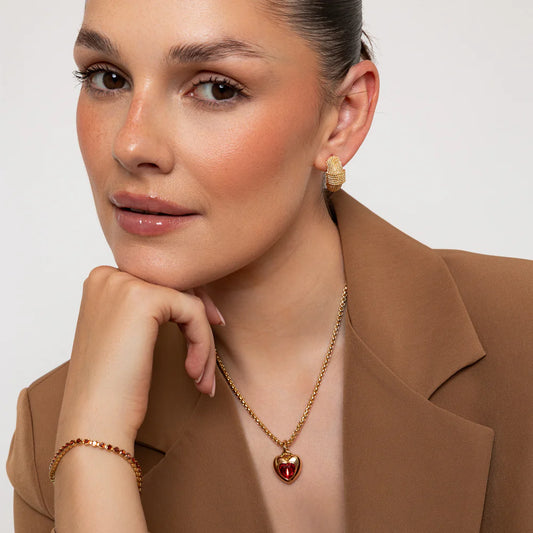Woman wearing gold jewelry including earrings, necklace, and bracelet against a neutral background