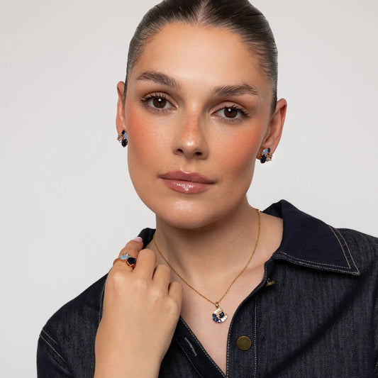 Woman wearing jewelry including earrings, a necklace, and a ring on a plain background