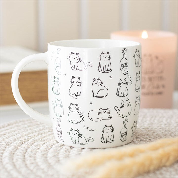 White mug with black cat illustrations on a textured surface with a candle in the background