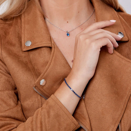 Person wearing a brown jacket with a necklace and bracelet, focusing on jewelry details.