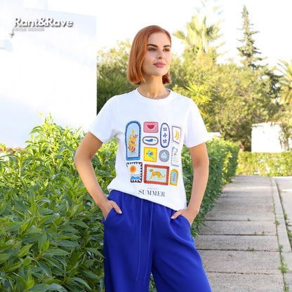 Woman wearing a white t-shirt with colorful graphics and blue pants standing outdoors.