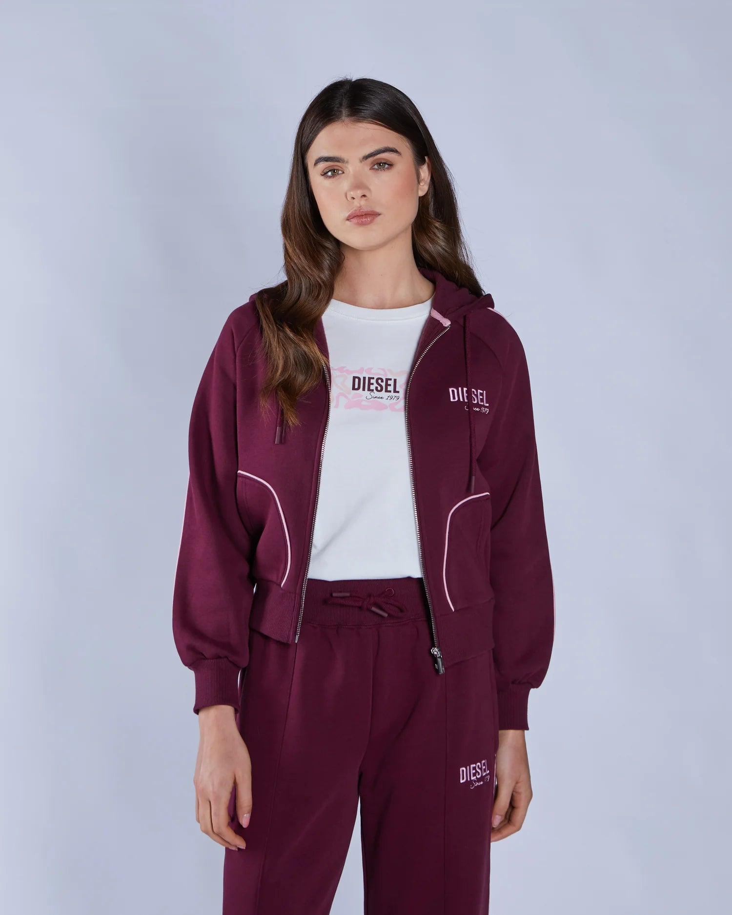 Woman wearing a burgundy tracksuit with 'DIESEL' branding on a light gray background
