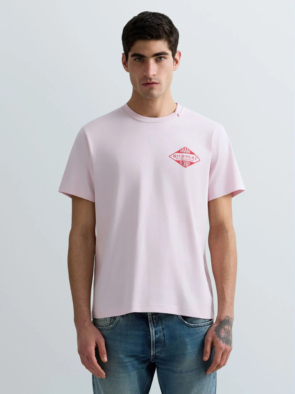 Man wearing a light pink t-shirt with a red logo on a plain background