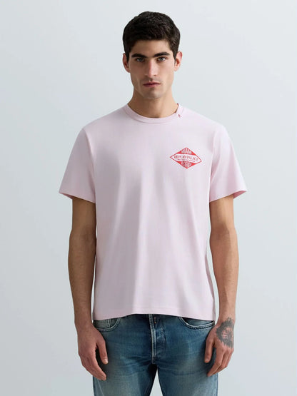 Man wearing a light pink t-shirt with a red logo on a plain background
