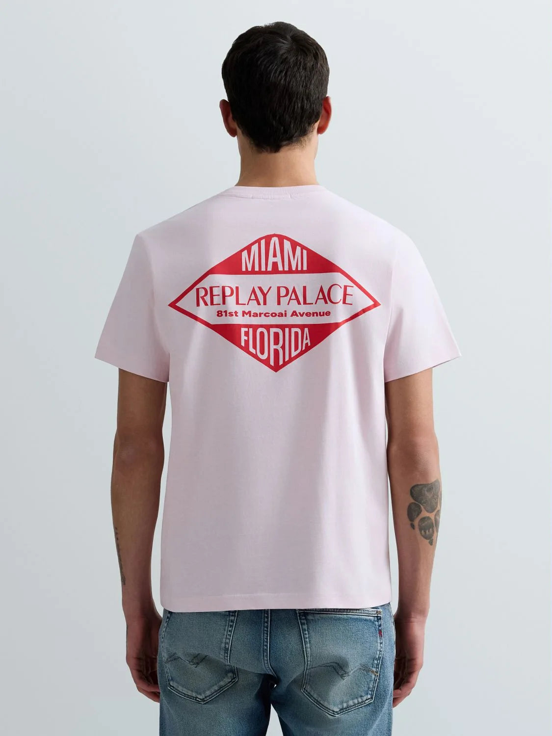 Person wearing a light pink t-shirt with a red and black graphic on the back, standing against a plain background.