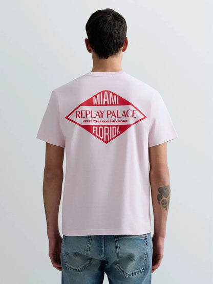 Person wearing a light pink t-shirt with a red and black graphic on the back, standing against a plain background.