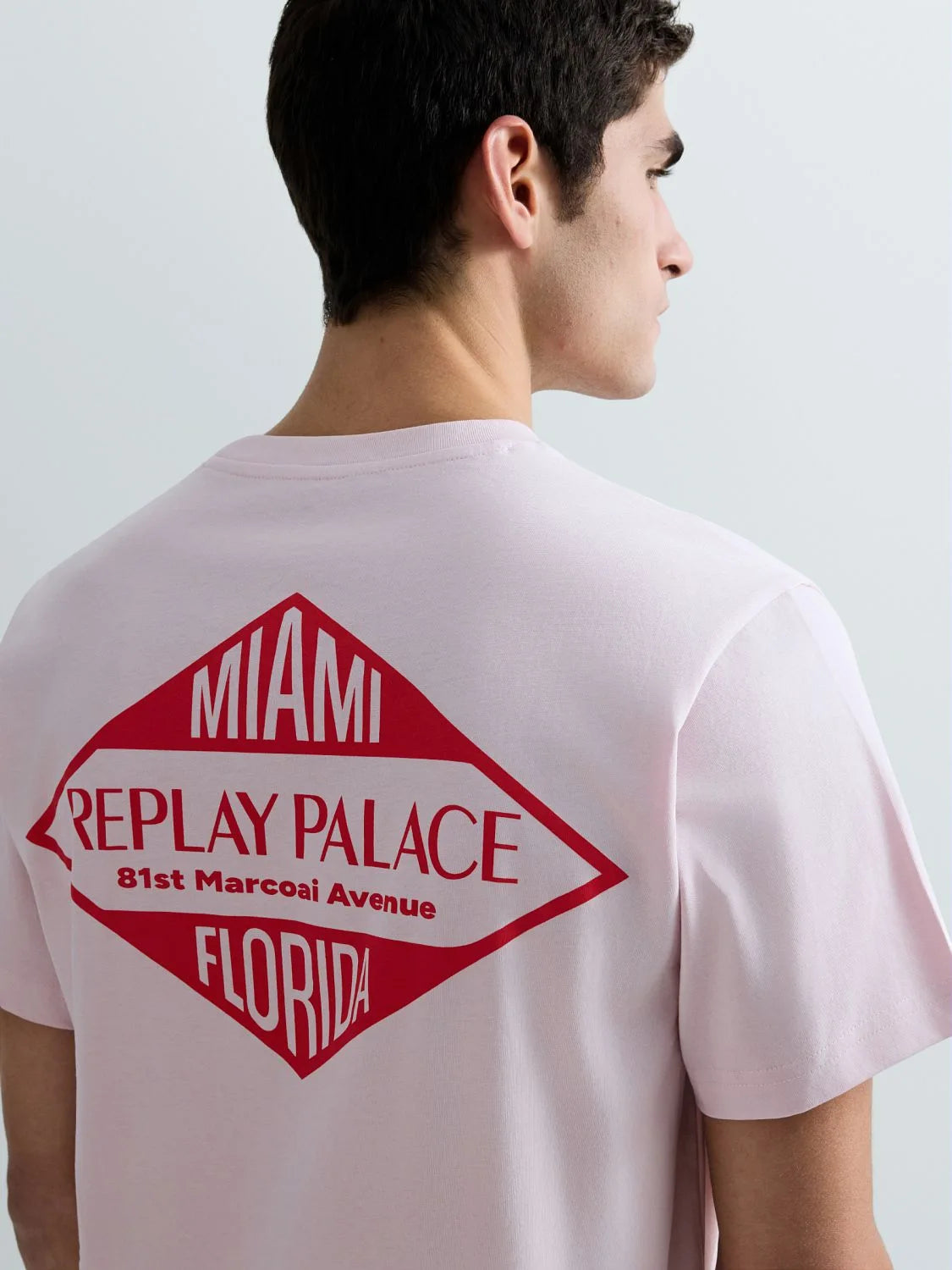 Person wearing a light pink t-shirt with a red and white graphic on the back, featuring text.