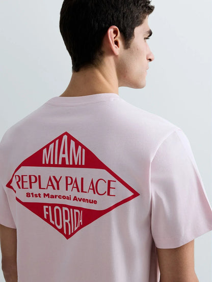 Person wearing a light pink t-shirt with a red and white graphic on the back, featuring text.