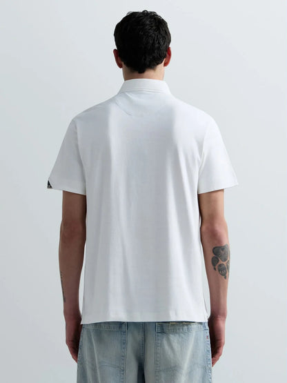 A man viewed from behind wearing a white short-sleeve polo shirt and light blue jeans against a plain light gray studio background.