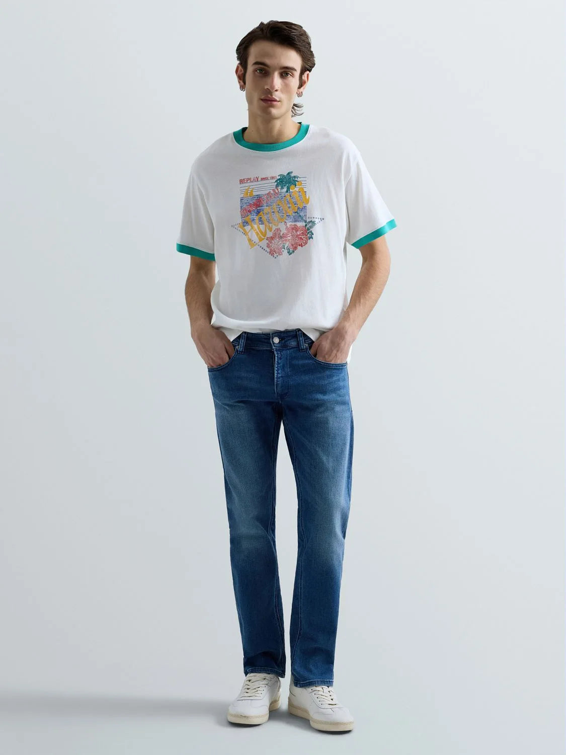 Man wearing a white t-shirt with colorful graphics and blue jeans on a light gray background