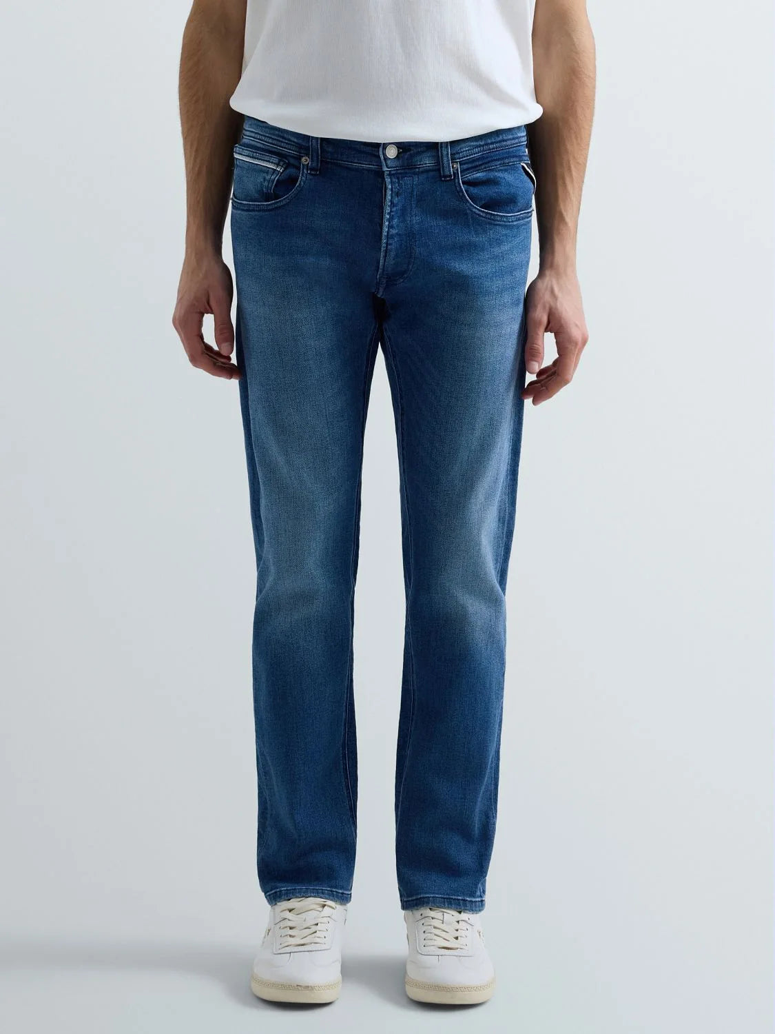 Person wearing blue jeans and a white shirt on a light gray background