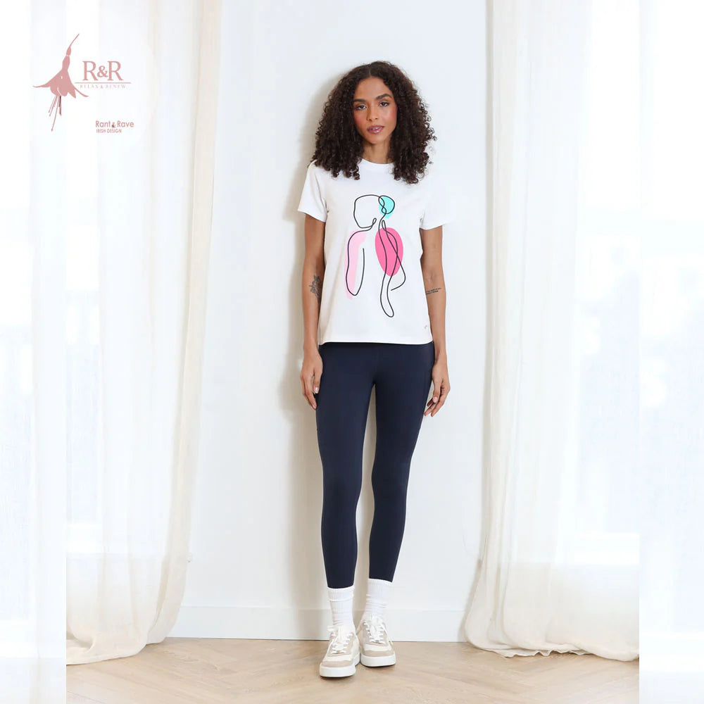Woman wearing a white t-shirt with a graphic design and navy leggings standing against a white curtain.