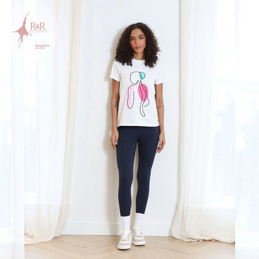 Woman wearing a white t-shirt with a graphic design and navy leggings standing against a white curtain.