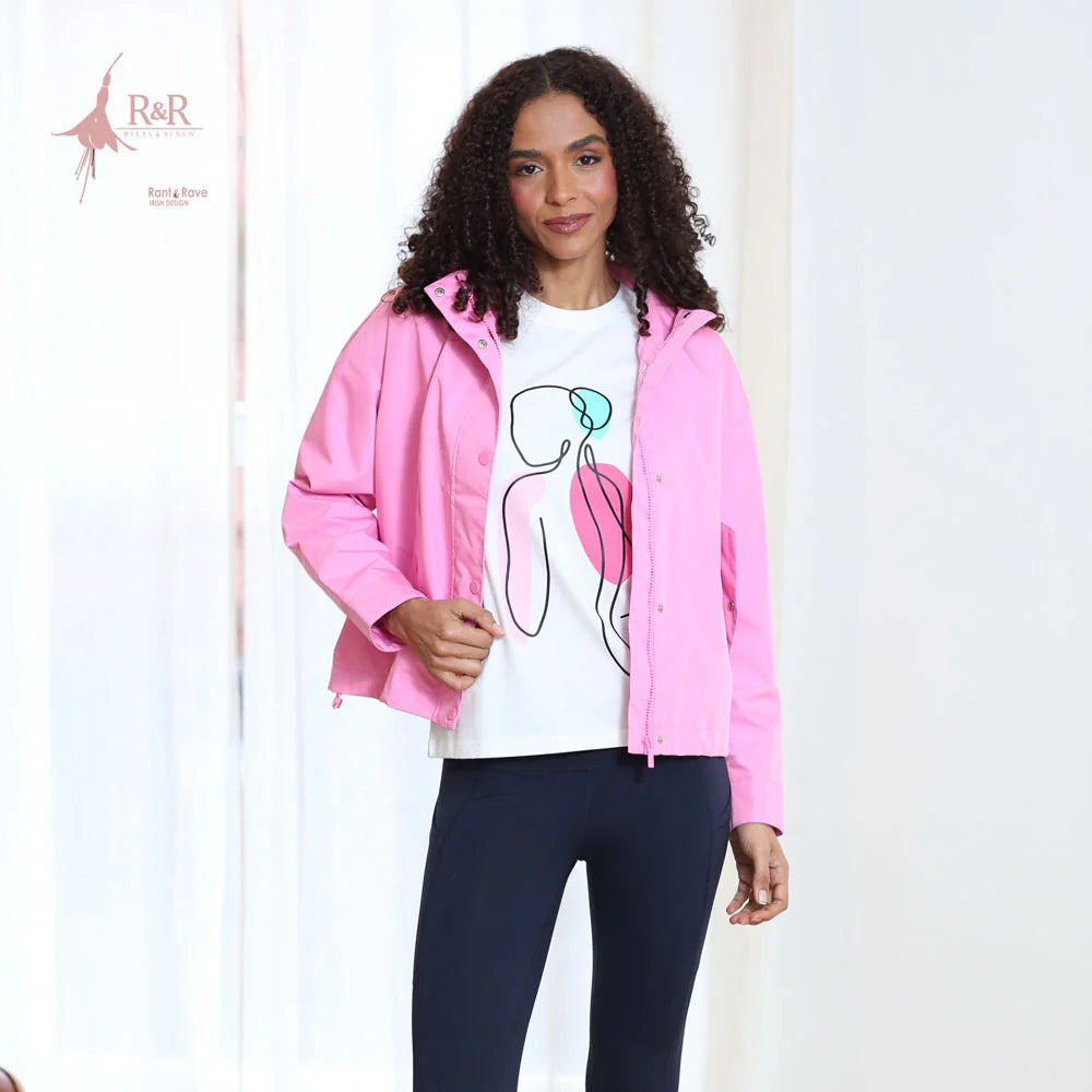 Woman wearing a pink jacket, white t-shirt with a graphic design, and dark pants on a white background.