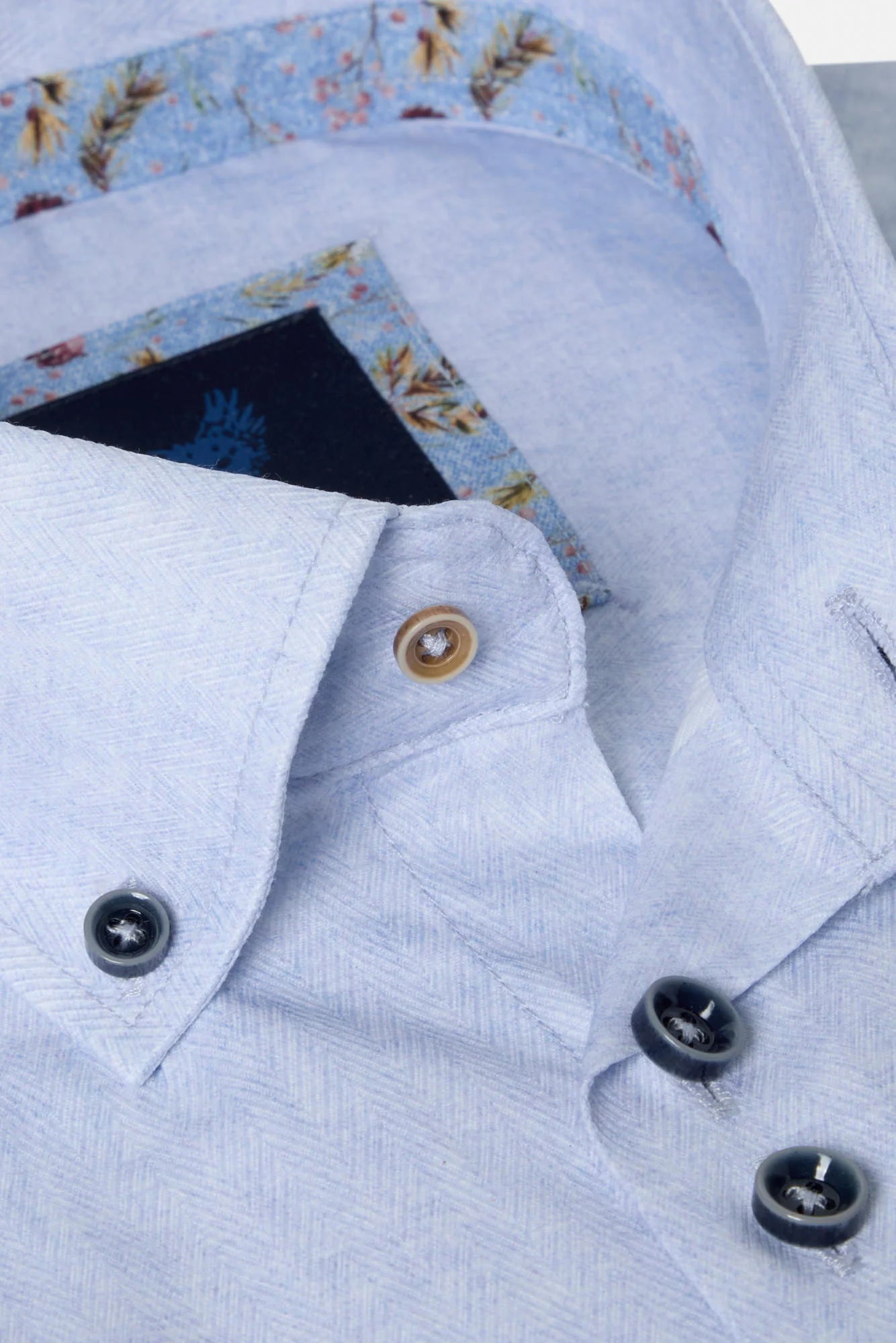 Close-up of a light blue shirt with buttons and a floral patterned fabric underneath.