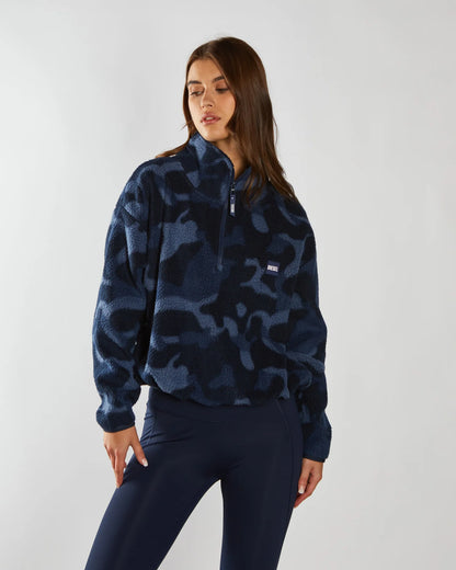 Person wearing a blue camouflage pullover with a brand logo on a white background