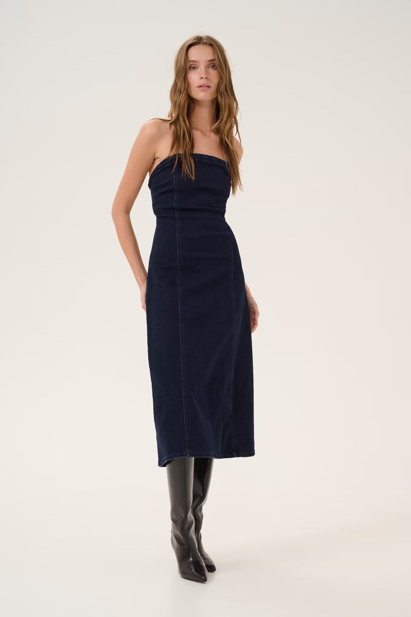 Woman wearing a strapless navy dress and black boots on a white background