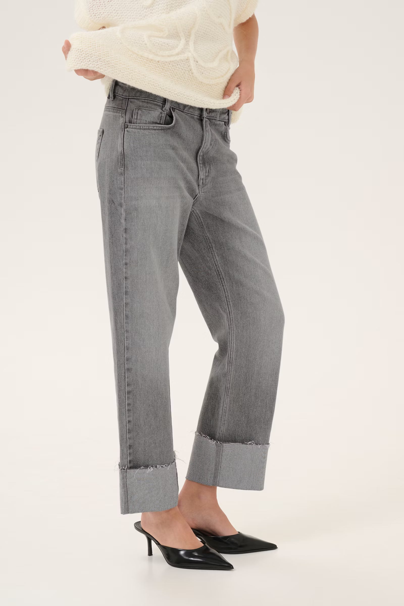 Person wearing gray jeans and a cream sweater on a white background