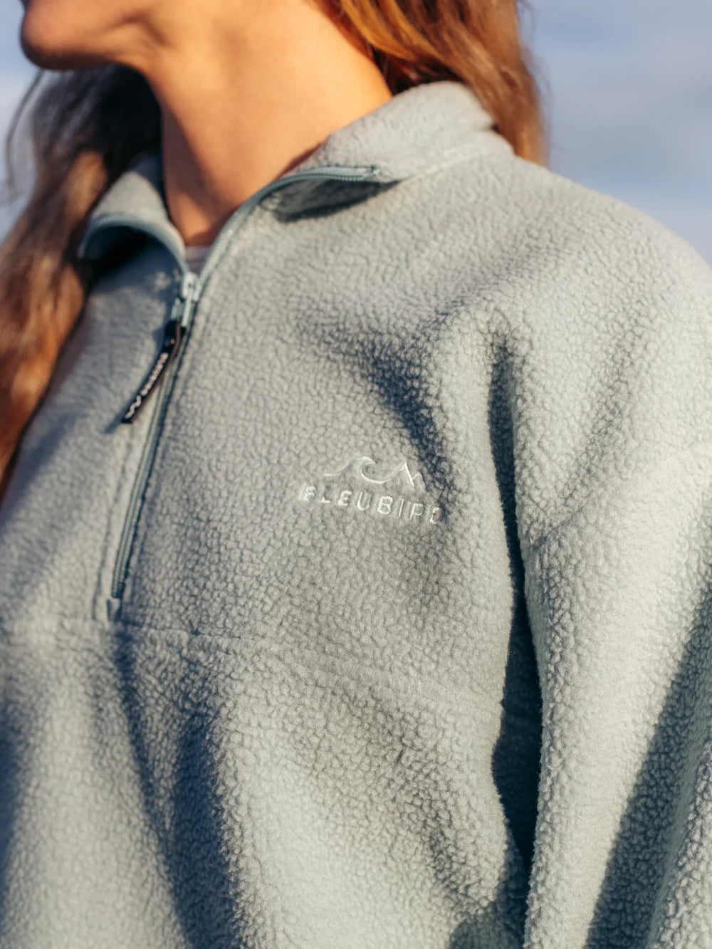 Close-up of a person wearing a gray fleece jacket with a brand logo on the chest.