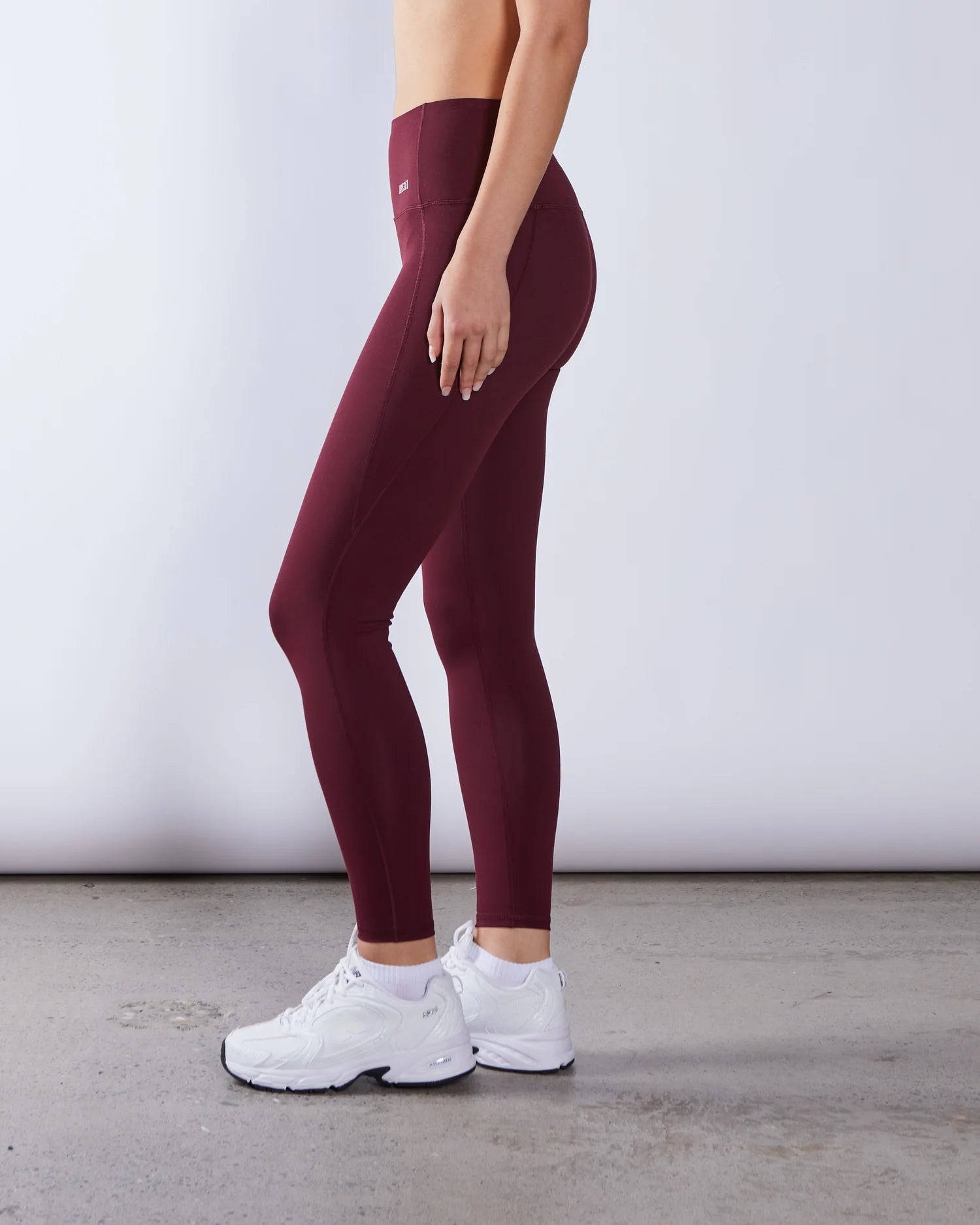 Person wearing maroon leggings and white sneakers on a plain background
