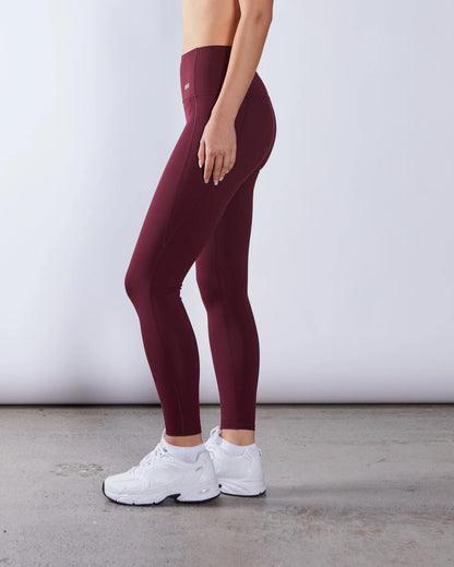 Person wearing maroon leggings and white sneakers on a plain background