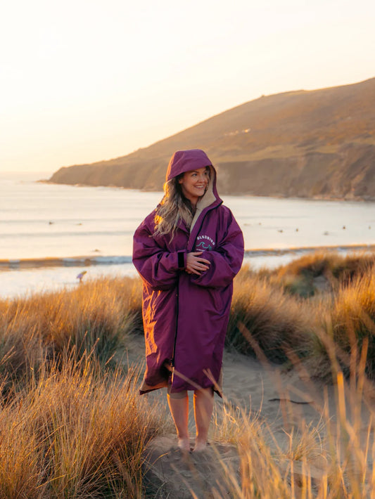 Person wearing a purple raincoat standing on a beach with a scenic background