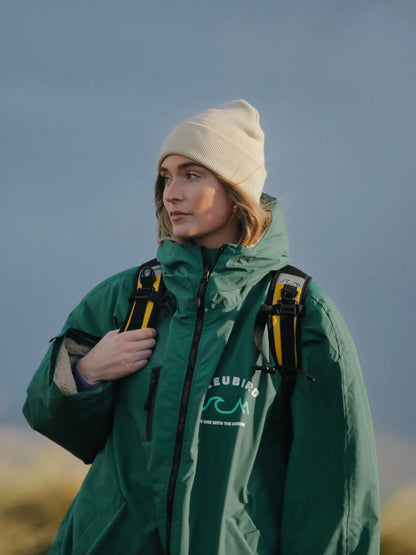 Person wearing a green jacket with a brand logo, standing outdoors against a blue sky.