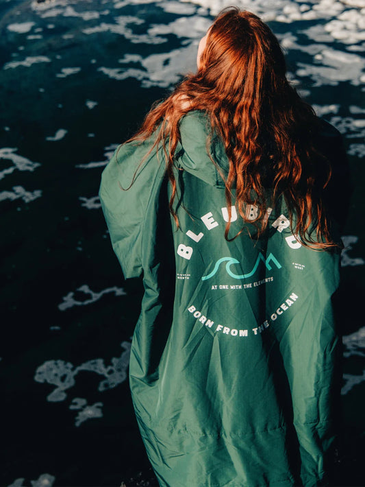Person wearing a green jacket with branding, standing by water