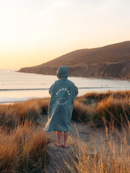 Person wearing a hooded jacket standing on a beach at sunset, with 'Silurian' branding visible.