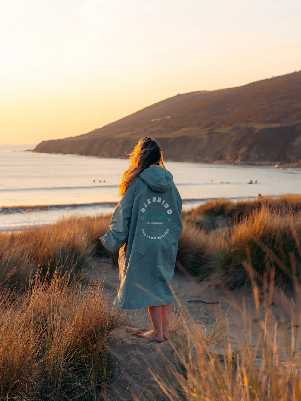 Person in a branded robe standing on a beach at sunset