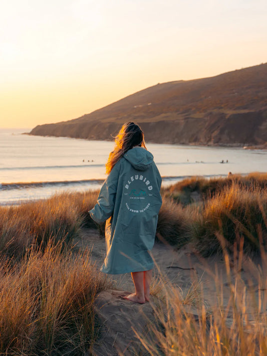 Person in a branded robe standing on a beach at sunset