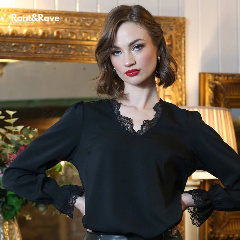 Woman wearing a black blouse with lace details in an elegant interior setting.