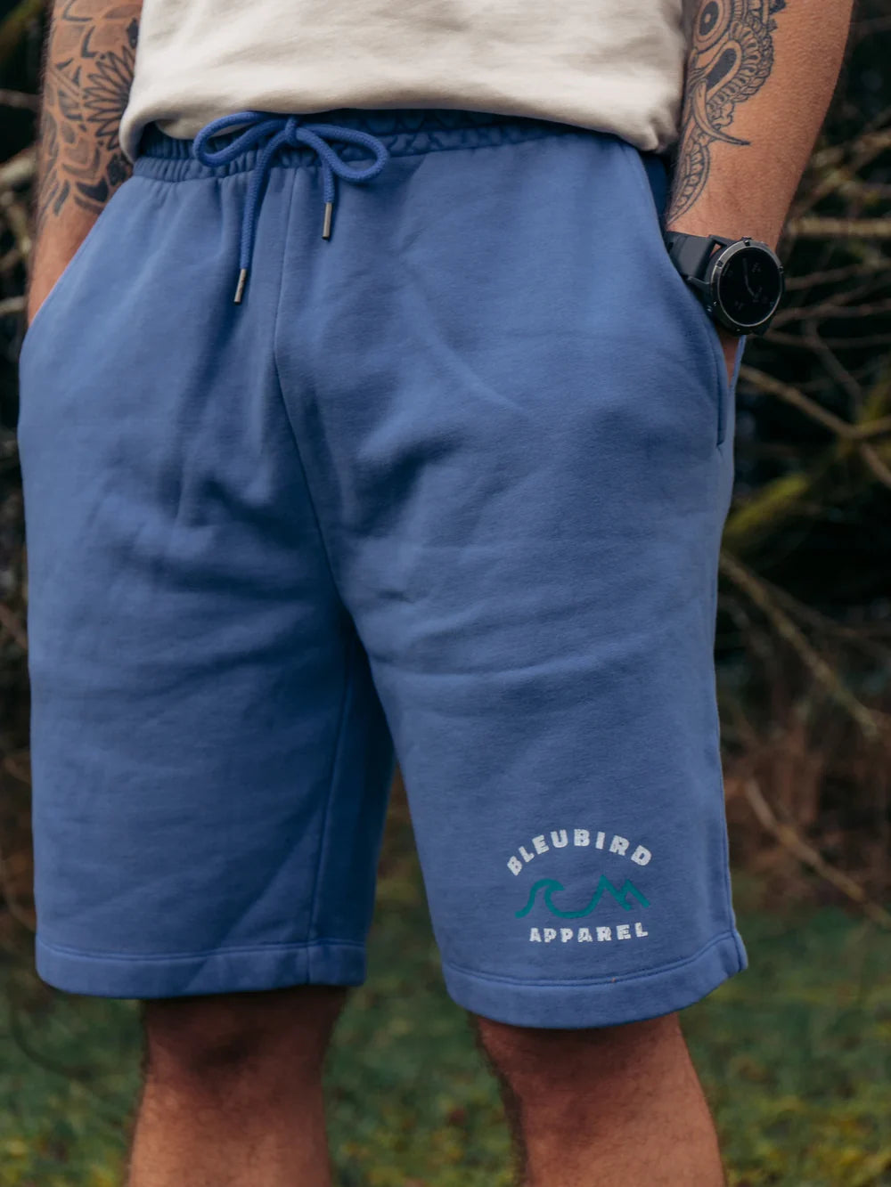 Person wearing blue shorts with a brand logo, standing outdoors.